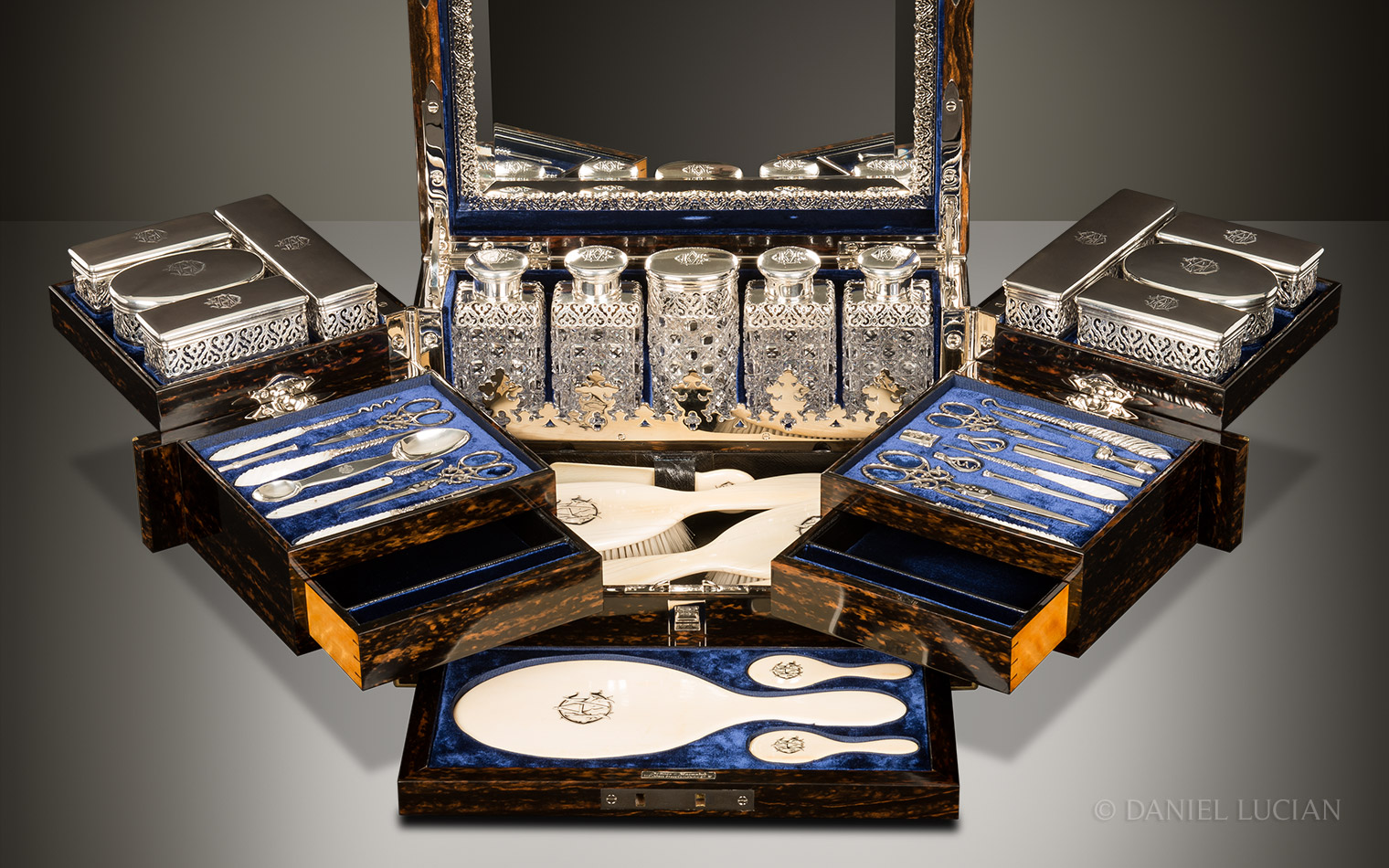 Closer front interior view of an antique dressing case in coromandel with Betjemann Patent mechanism, by Jenner & Knewstub, with the silver-mounted bottles and jars, vanity tools, and ivory hand mirrors and brushes on display.